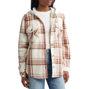 A woman is wearing a brown and white plaid flannel shirt jacket layered over a white top, paired with blue jeans.