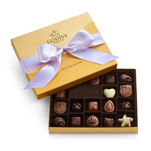 Godiva Gold Collection box featuring assorted chocolates with various shapes, including hearts and stars, tied with a light purple ribbon.