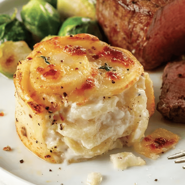 A plate featuring a serving of creamy potato gratin is accompanied by Brussels sprouts and a portion of steak.
