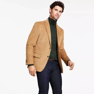 A man is wearing a tan blazer, dark green turtleneck, and navy jeans.