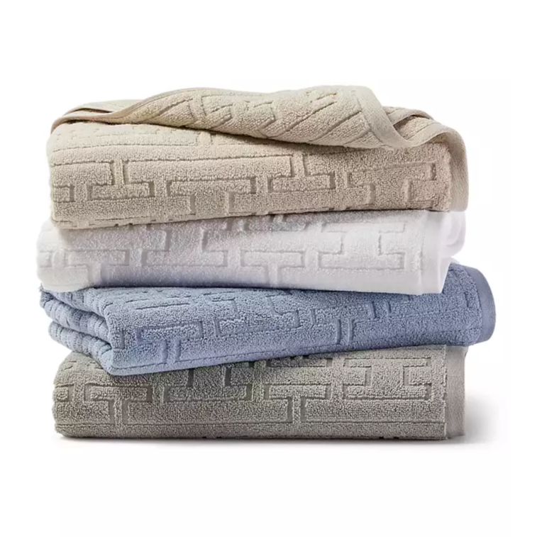 A stack of four folded towels in beige, white, blue, and gray, each with a geometric pattern.