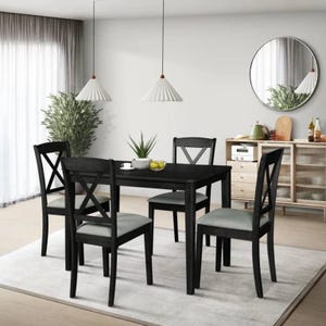 Dining set with a black table and four chairs on a white rug, featuring cross-back designs. Two pendant lights hang above, and there's a sideboard with decorative items against the wall. A round mirror and potted plant complete the room decor.