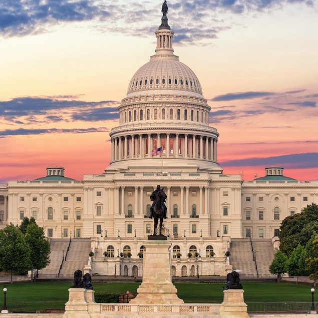 The U.S. Capitol building at sunset, featuring its iconic dome and an equestrian statue in the foreground, with a U.S. flag displayed prominently.