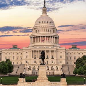 The U.S. Capitol building at sunset, featuring its iconic dome and an equestrian statue in the foreground, with a U.S. flag displayed prominently.