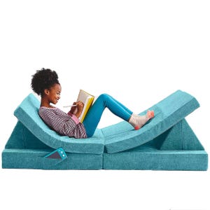 A woman is reclining on a blue modular foam couch, reading a book.
