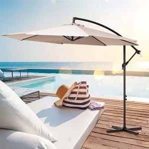 A 10' patio cantilever umbrella with a sturdy metal stand is shown beside a pool, offering shade to a lounger that features a striped bag and a straw hat, set against a serene ocean view.