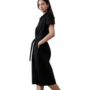 A black midi-length shirtdress with short sleeves, featuring a tie waist for adjustable fit and a collared neckline. It has a simple, elegant design suitable for various occasions.