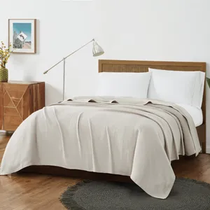 A cozy bedroom with a beige blanket on a wooden bed, white pillows, a mid-century modern nightstand, a metal floor lamp, a woven rug, and potted plants by a window.