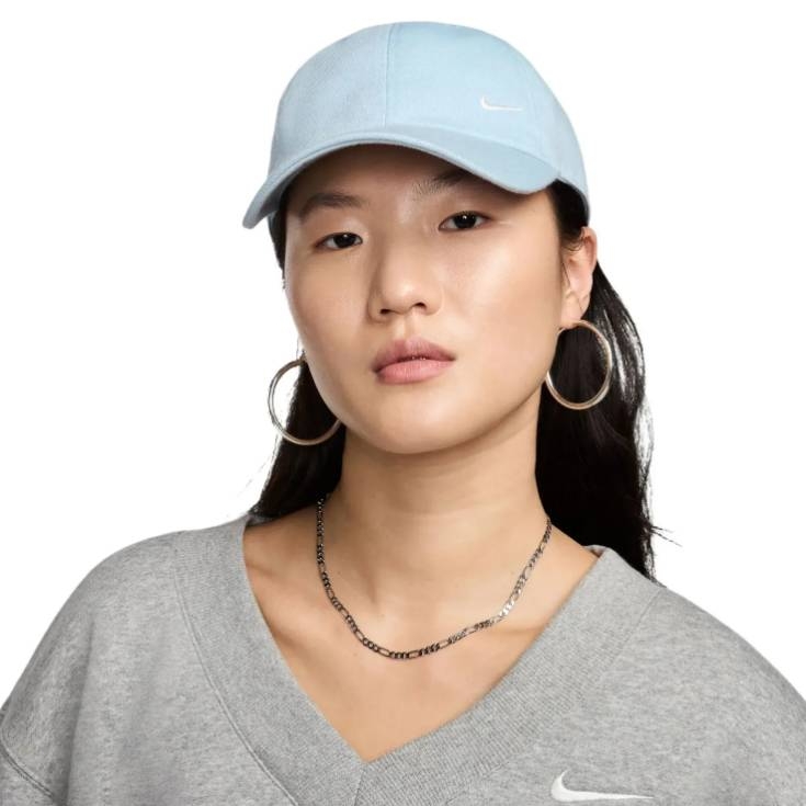 A person is wearing a light blue Nike baseball cap, a gray Nike sweatshirt, large hoop earrings, and a thin chain necklace.