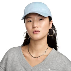 A person is wearing a light blue Nike baseball cap, a gray Nike sweatshirt, large hoop earrings, and a thin chain necklace.