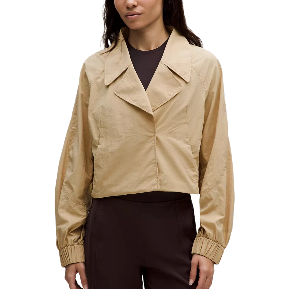 A beige cropped jacket with a wide collar, long sleeves, and elastic cuffs, paired with dark, high-waisted pants.