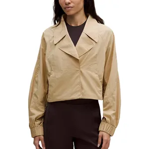 A beige cropped jacket with a wide collar, long sleeves, and elastic cuffs, paired with dark, high-waisted pants.