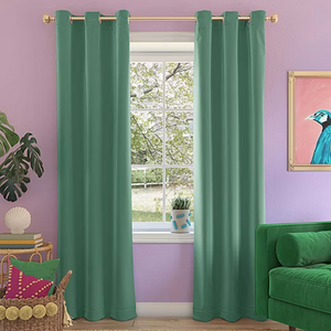 A teal energy-saving blackout curtain panel hangs from a gold rod against a lavender wall, effectively blocking light. It complements the room's decor, which includes a green couch, potted plant, and vibrant pillows.