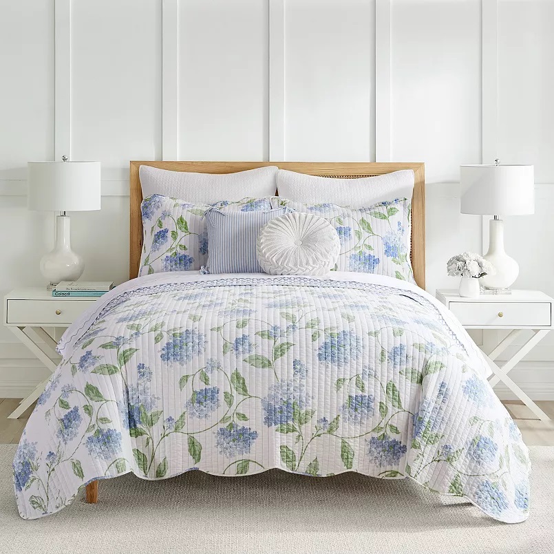 A floral-patterned quilt set with coordinating pillows on a bed, flanked by two white table lamps.