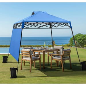 An 8' x 8' blue pop-up canopy provides shade over a wooden outdoor dining set with four cushioned chairs on a grassy lawn, with a pool and ocean visible in the background.