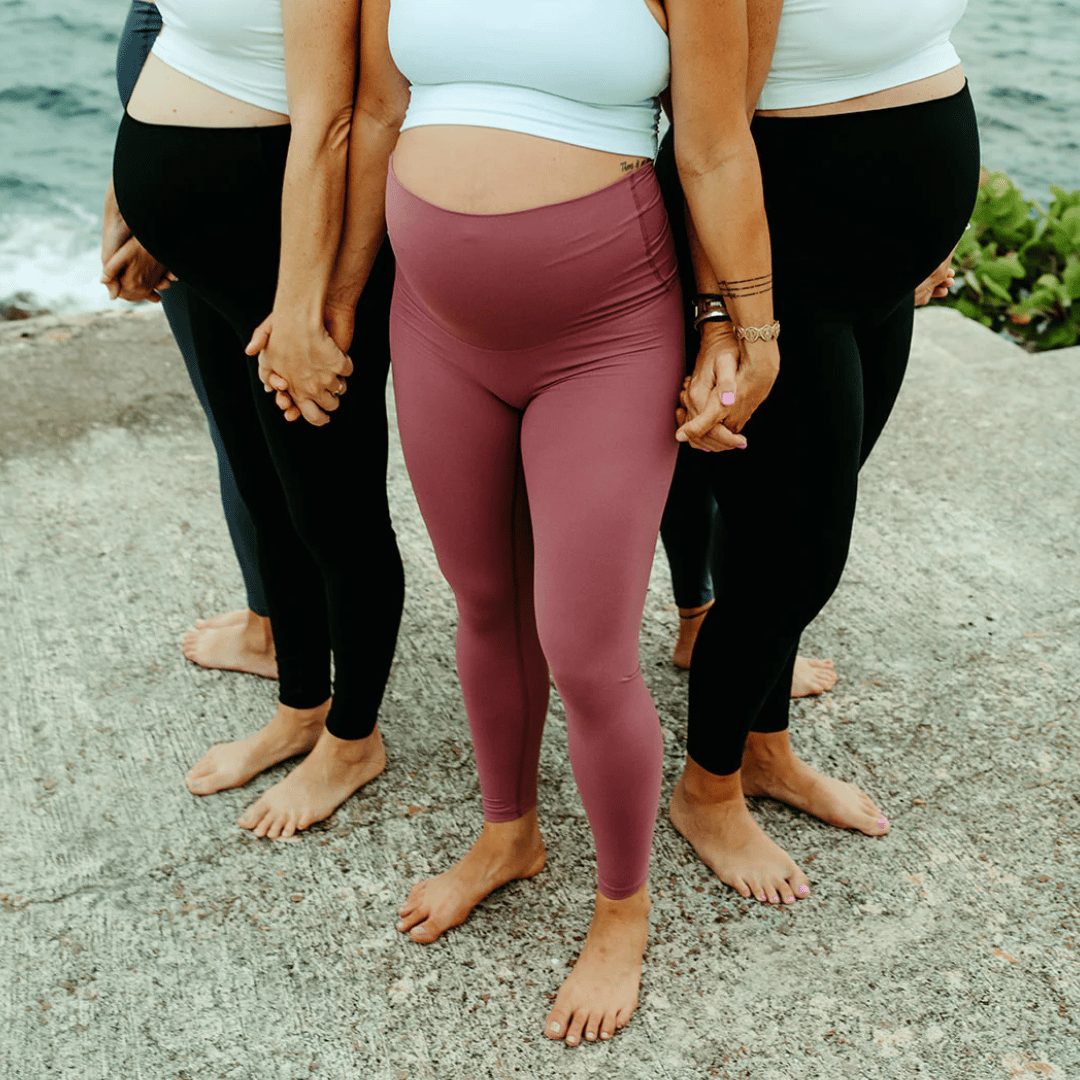 Pregnant individuals wearing various styles of leggings and crop tops, standing barefoot on a concrete surface by the water.