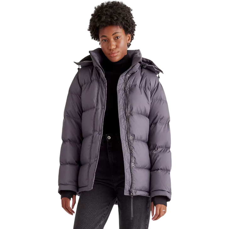 A person is wearing a dark gray puffer jacket with a hood, styled over a black turtleneck and dark jeans. The jacket features a quilted design and front zipper closure, with a highlighted discount offer above.