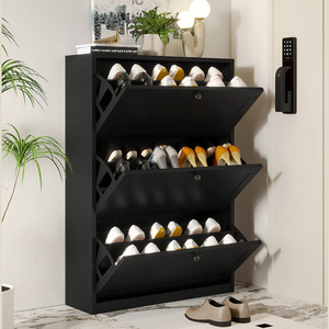 Black shoe storage cabinet with three drop-down compartments, holding multiple pairs of shoes. Decor includes plants and a lamp on top, with a nearby electronic door lock.
