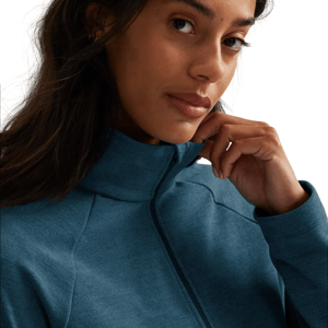 A person wears a teal zip-up jacket with a high collar, holding the collar slightly open with their fingers.