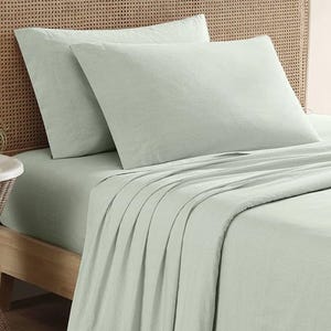 Tommy Bahama Cotton Queen Sheet Set features light mint green sheets with a subtle textured pattern, including a fitted sheet, flat sheet, and two pillowcases. The set is displayed on a bed with a wicker headboard.