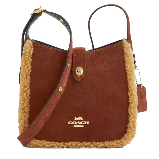 Coach shoulder bag with brown suede, gold logo, and shearling trim. Features adjustable strap and flap closure with gold snap button.