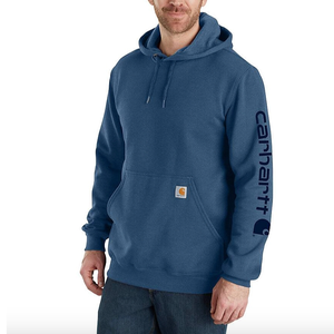 A man is wearing a blue Carhartt hoodie with the brand's logo on the left sleeve and a front pocket.