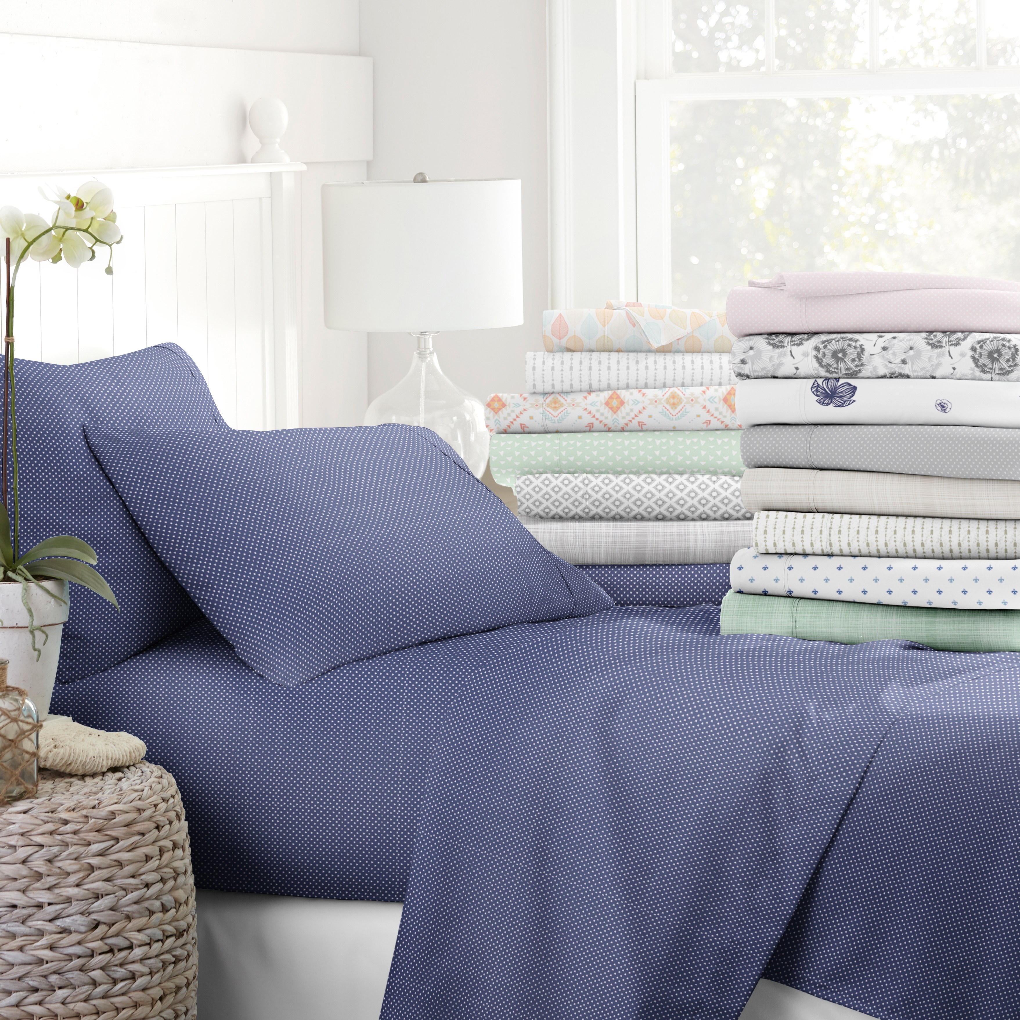 Bed adorned with blue dotted sheets and a variety of folded patterned beddings stacked beside it.