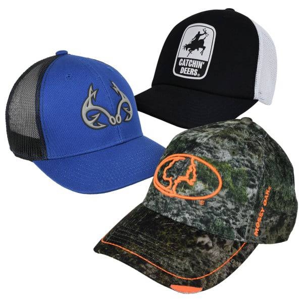 Three baseball caps are displayed: a blue cap with an antler logo, a black and white mesh cap with \“Catchin' Deers\“ text and graphic, and a camo cap with an orange logo and the \“Mossy Oak\“ branding.