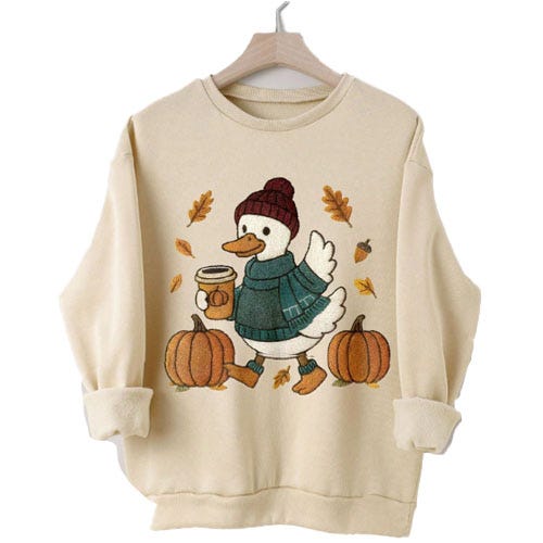 Sweatshirt featuring a cartoon duck wearing a beanie and scarf, holding a coffee cup, surrounded by pumpkins and autumn leaves.