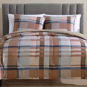 A plaid-patterned comforter set with matching pillows on a bed with a gray upholstered headboard. The design features various shades of brown, white, and blue.