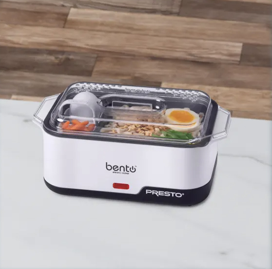 A portable electric lunch box with a transparent lid containing cooked rice, boiled egg, and vegetables. Branding shows \“bentō PRESTO\“.