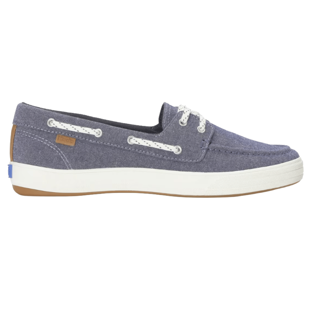 Casual boat shoe in chambray blue with white laces, grommet details, and a white rubber sole featuring a gum outsole.