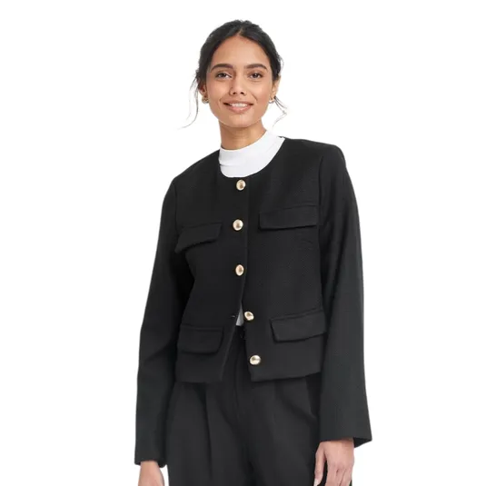 A woman is wearing a black button-up jacket with gold buttons, featuring two chest and two lower pockets, over a white top, paired with black pants.