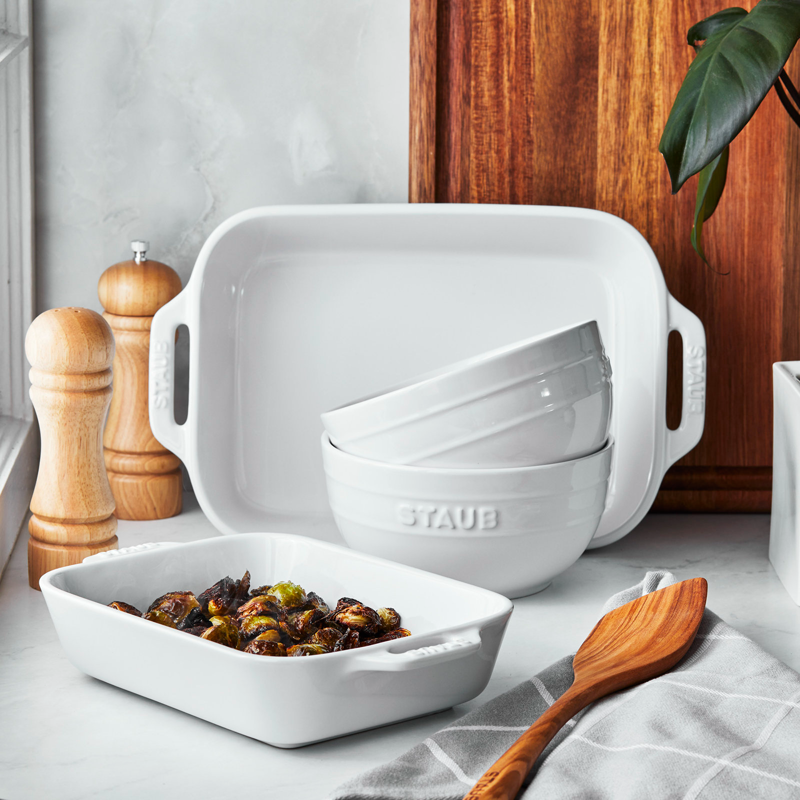 White ceramic bakeware, bowls stacked, wooden utensils, and salt and pepper grinders on a kitchen counter.