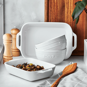 White ceramic bakeware, bowls stacked, wooden utensils, and salt and pepper grinders on a kitchen counter.