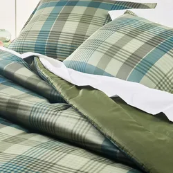 A bedding set featuring a green and blue plaid pattern with plain green backing, including matching pillowcases and white sheets.