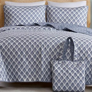 A bed is styled with a blue and white patterned quilt and pillow shams, complemented by a matching tote bag.