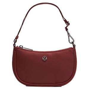 A small, maroon handbag with an adjustable strap and a metal emblem on the front. The bag features a zipper closure and a detachable hook.