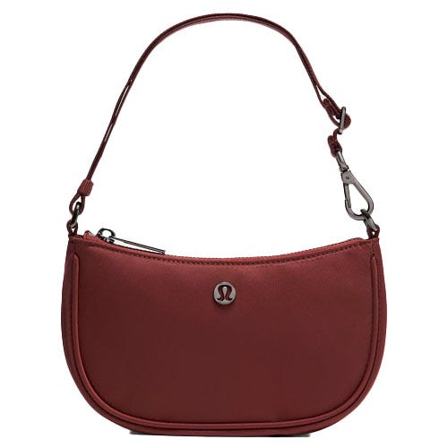A small, maroon handbag with an adjustable strap and a metal emblem on the front. The bag features a zipper closure and a detachable hook.