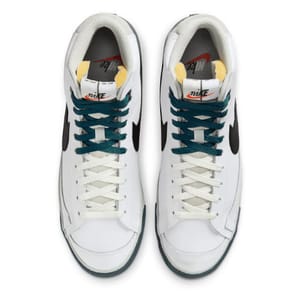 A pair of white Nike sneakers with navy and light green accents, viewed from above.