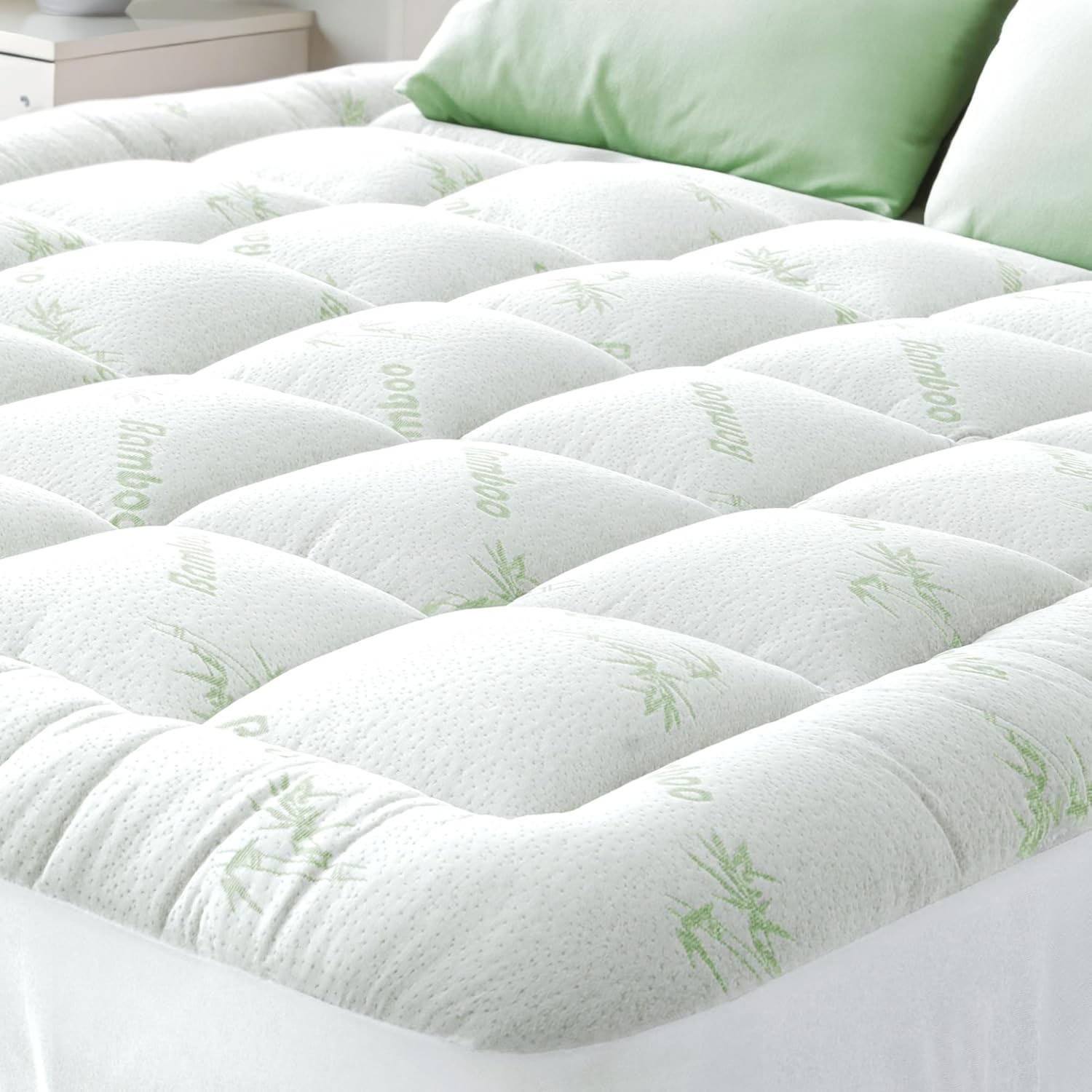A quilted bamboo mattress topper enhances comfort with its padded design, featuring green bamboo patterns on a white surface, paired with matching green pillows.