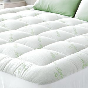 A quilted bamboo mattress topper enhances comfort with its padded design, featuring green bamboo patterns on a white surface, paired with matching green pillows.