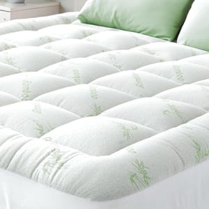 A quilted bamboo mattress topper enhances comfort with its padded design, featuring green bamboo patterns on a white surface, paired with matching green pillows.