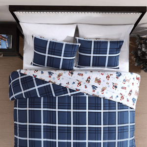 A bed is made up with a blue plaid comforter and matching pillow shams. The bedding is turned to reveal a fun, holiday-themed bedsheet with snowmen and reindeer.