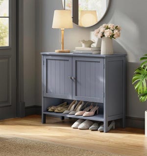 Gray shoe storage cabinet with two doors and an open lower shelf displaying several pairs of shoes.