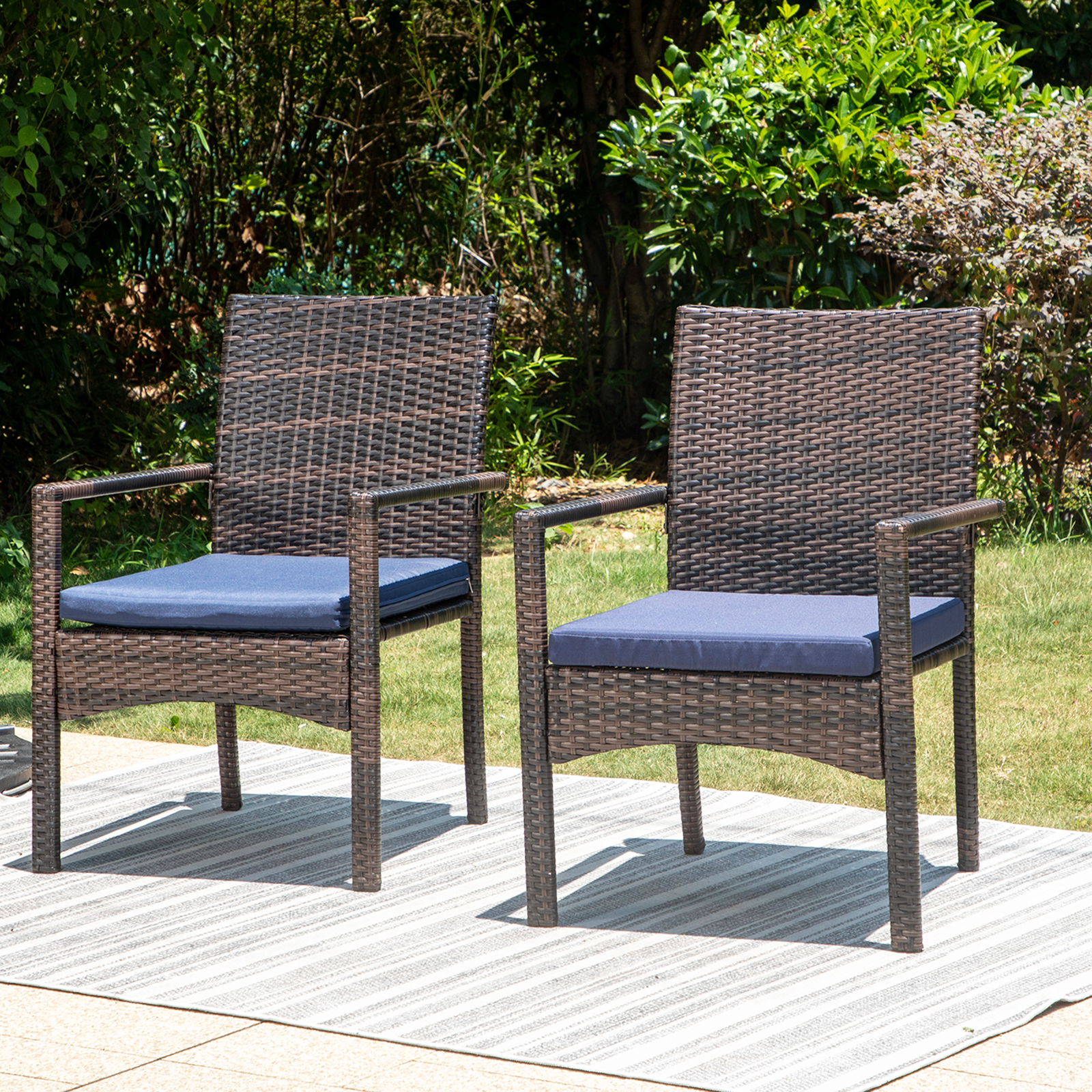 Two brown wicker chairs with blue cushions on an outdoor patio rug.