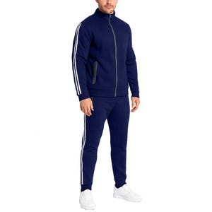 A man is wearing a navy blue tracksuit with white stripes along the sleeves and pants, paired with white sneakers.