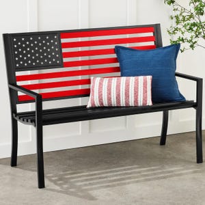 A black bench with an American flag design features a red and white striped pillow and a blue pillow.
