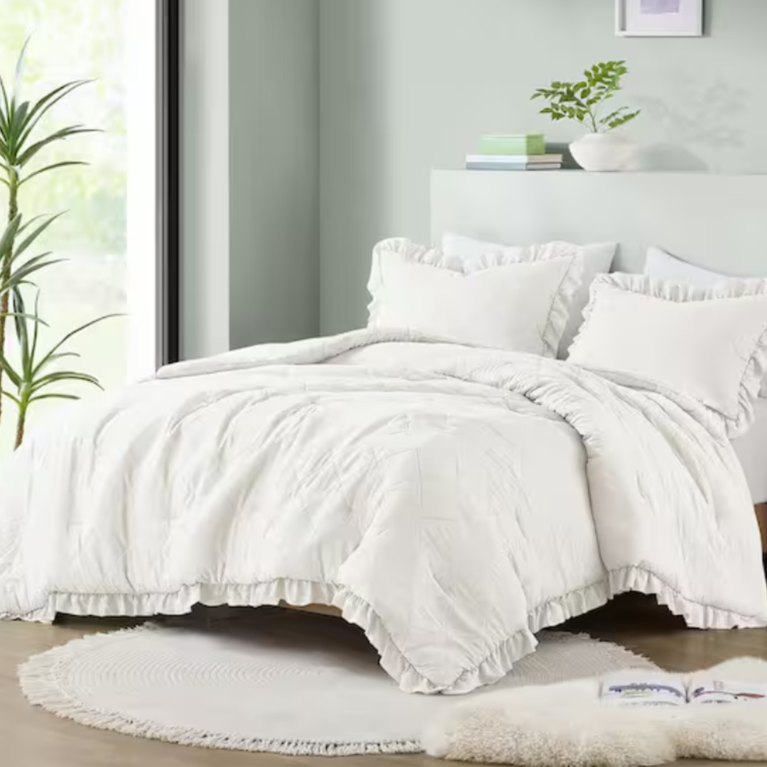 A white ruffled bedding set with comforter and multiple pillows on a bed, with a circular rug at the foot.