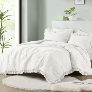 A white ruffled bedding set with comforter and multiple pillows on a bed, with a circular rug at the foot.